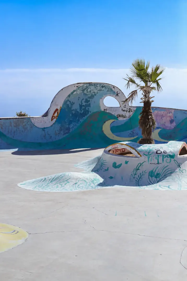 Skatepark bowl painted with a giant ocean wave mural and a palm tree under a blue sky near Taghazout and Tamraght, Morocco